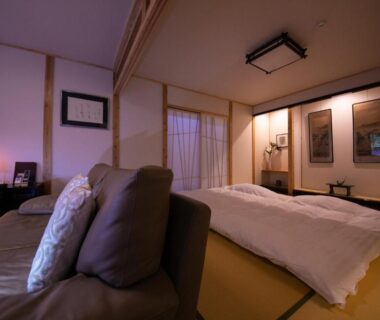 Traditional tatami room with futon mattress, low sofa seating, shoji screens and warm ambient lighting at Oyado Den Rikyu