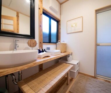 Sink on wooden counter with mirror, woven bench and frosted sliding door in Oyado Den Rikyu washroom, Ōita