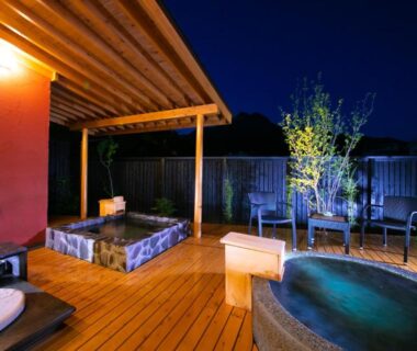 Wooden deck with stone soaking tubs and seating under night sky at Oyado Den Rikyu, Ōita