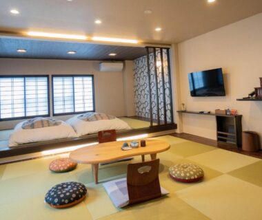 Japanese tatami room with low wooden table, zabuton cushions, raised futon bedding area and shoji screens at Oyado Eitaro, Gifu