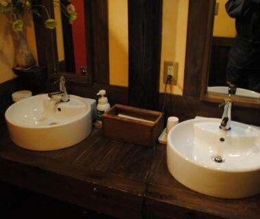 Two round ceramic sinks on dark wooden counter with mirrors and soap at a ryokan bathroom, Tochigi