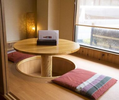 Tatami room with sunken round table and floor cushions by window at Oyado Ichifuji, Tochigi