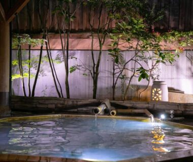 Heated wooden onsen pool with bamboo screen and soft lantern lighting at Oyado Ichizen in Ōita Kyūshū