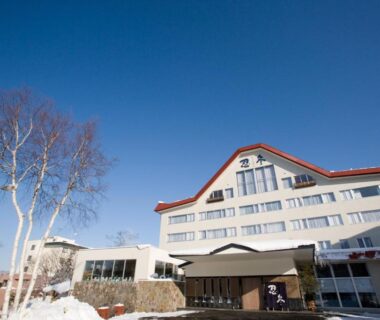 Multi story ryokan building with snow at entrance, birch trees and clear blue sky in Hokkaidō