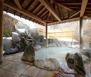 Covered rock-lined onsen bath with wooden roof and bamboo fence at Oyado Kiyomizuya Hokkaidō