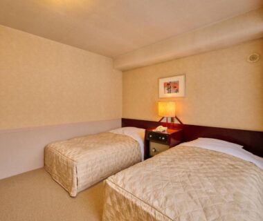 Two single beds with bedside lamp in compact room at Oyado Kiyomizuya Hokkaidō