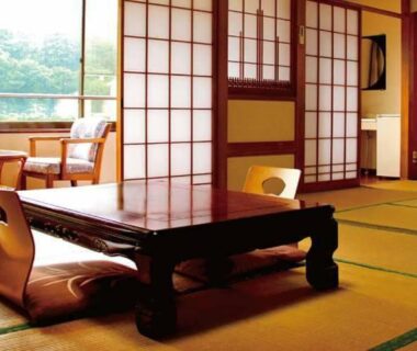 Tatami room with low table, shoji screens and seating by window overlooking greenery at Oyado Matsubaya, Gunma