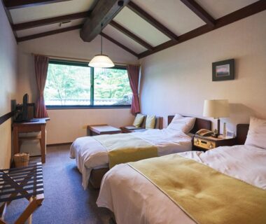 Twin beds, exposed wood beams, low table by window with green garden view and luggage rack