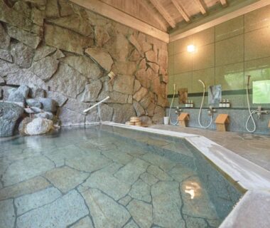 Indoor stone-walled onsen bath with shower stations and wooden stools at Oyado Nagomino in Nagano