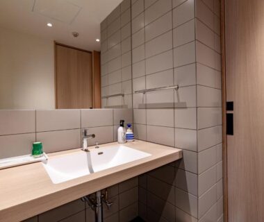 Minimal bathroom sink and mirror with tiled wall and wooden door at Oyado Seri Hyōgo