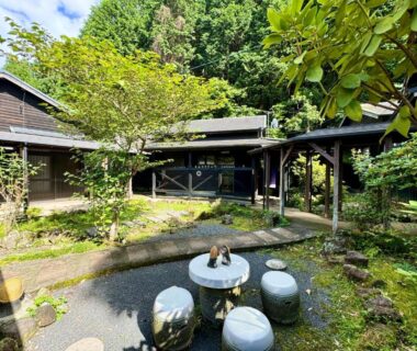 Traditional ryokan courtyard with stone table and stools, moss, wooden walkways and lush greenery at Oyado Tamayura in Ōita