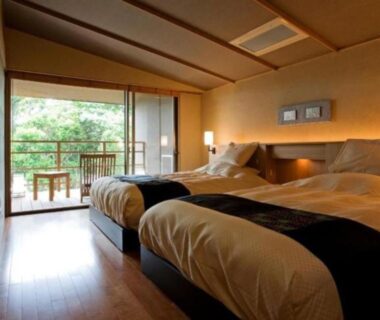 Twin beds in ryokan room with wooden floor, shoji doors and balcony view of greenery at Oyado The Earth Mie