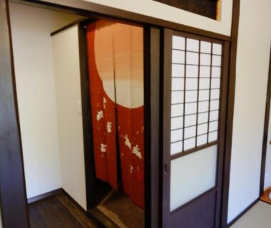 Interior doorway with red noren and shoji screens leading into tatami area at Oyado Tsukiusagi, Hiroshima