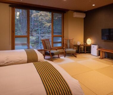 Tatami-floor room with two beds, low seating by window and wall-mounted TV at Oyado Tsuruya