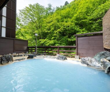 Milky blue outdoor onsen bath with rock edging and forest backdrop at Oyado Tsuruya Nagano