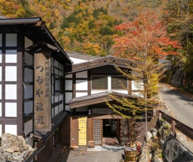 Exterior of Oyado Tsuruya with white plaster and timber facade, stone steps and autumn foliage in Nagano mountains