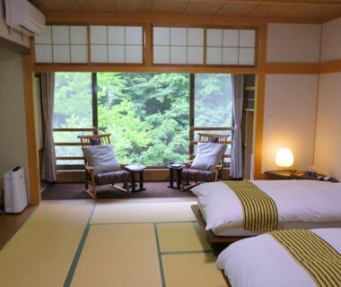 Tatami room with twin low beds, shoji screens and seating overlooking green garden at Oyado Tsuruya, Nagano