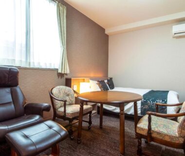 Room seating area with leather recliner, round wooden table, upholstered chairs and single bed in a carpeted room