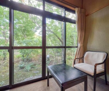 Seating with chair and low table by large window overlooking green trees at Oyado Yumechidori in Saga