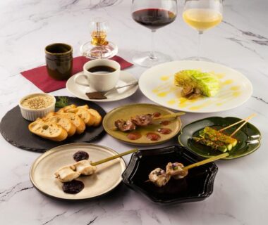 Assorted small plates and skewered bites with wine glasses and coffee on a marble table at a ryokan dining setting