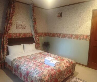 Double bed with floral bedspread, canopy and folded towels at Pension Balmy in Tochigi