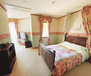 Western-style guest room with wooden bed, floral bedding, curtains and television at Pension Balmy, Tochigi