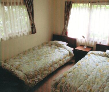 Two single beds with bedside table and bright windows at Pension Hakuba 70 in Nagano Chubu