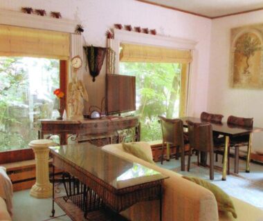 Bright lounge with sofas, wooden tables and large garden-view windows at Pension Hakuba 70, Nagano Chūbu Japan
