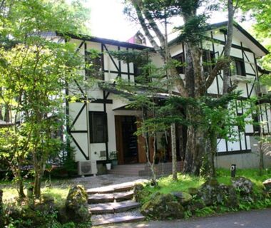 White timber-framed pension building of Pension Marie among trees with stone path in Yamanashi, Chūbu