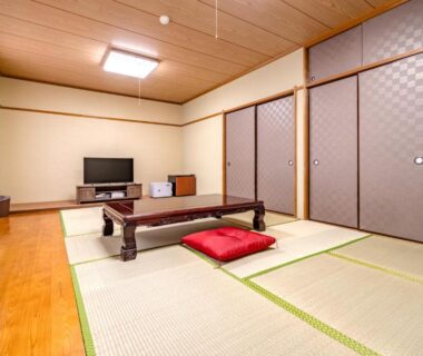Spacious tatami room with low table, red zabuton cushion, sliding doors and television at PiDDs Family 熱海, Shizuoka