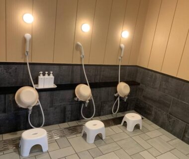 Three seated washing stations with stools and handheld showers in a ryokan bath area in Hokkaidō
