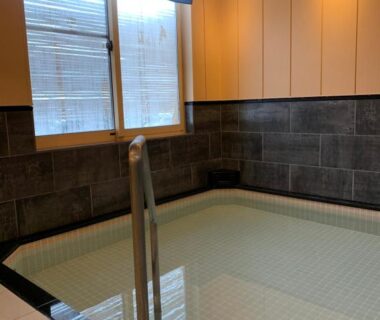 Tiled indoor bath with handrail, noren curtains and wooden wall panels at Plum House Otaru, Hokkaidō