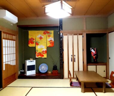 Traditional tatami room with low table, zabuton cushions, shoji screens, tokonoma alcove and small television at Plum House Otaru Hokkaidō