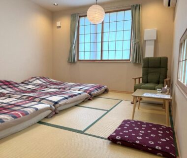 Japanese tatami room with futon bedding, low table, cushion and window at Plum House Otaru in Hokkaido
