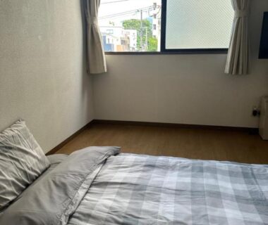 Low bed with gray checked bedding on wooden floor at Private Inn Bambee in Hyōgo, small city view