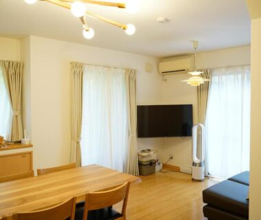 Light-filled living area with wooden dining table, sofa and flat-screen TV at MIYAJIMA tonbo-AND in Hiroshima