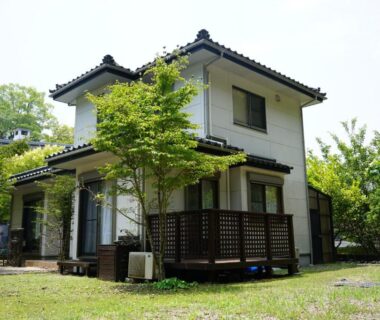 Two-story house with wooden deck and grassy yard at Private stay MIYAJIMA tonbo-AND Hiroshima