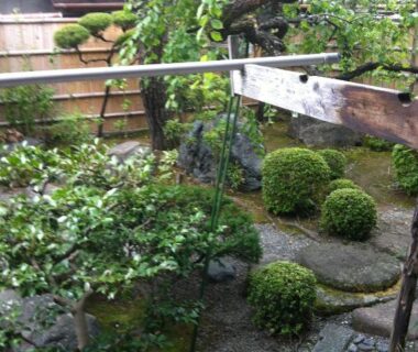 Enclosed Japanese garden with gravel path, stone stepping stones, trimmed moss mounds and wooden fence at Rakucho Ryokan Kyoto