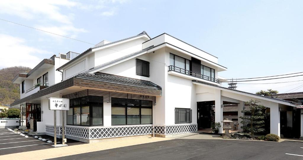 Exterior view Rakusuien Yamanashi Japan White two-story ryokan building with covered entrance, parking area and low hills in the background