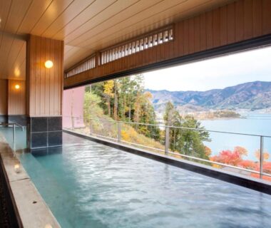 Indoor onsen bath with panoramic window overlooking lake and mountains at Rakuyu in Yamanashi, Chūbu, Japan