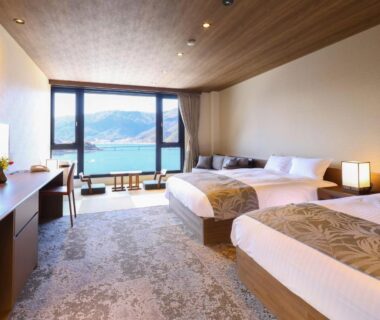 Twin beds, low wooden table by floor-to-ceiling window overlooking lake and mountains at Rakuyu in Yamanashi