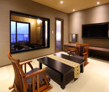 Tatami room with low table, wooden chairs, wall TV and large window at Rakuyu, Yamanashi