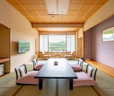 Spacious tatami room with low dining table, floor cushions, shoji screens and green hillside view at Rantei, Miyagi