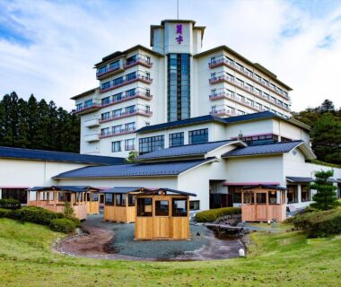 Multi-story ryokan building with wooden outdoor pavilions, lawn and tree-lined hillside in Miyagi, Tōhoku