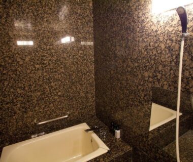 Dark tiled bathroom at Ranzan ryokan in Kyoto with bathtub and handheld shower