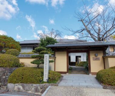 Stone entrance path with manicured shrubs, low eaves and tiled roof at Ranzan ryokan Kyoto