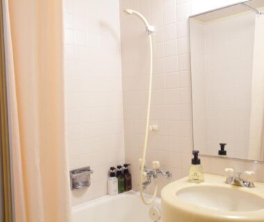Small bathroom with tub, shower, sink, mirror and toiletries at Ranzan in Kyoto