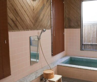 Indoor soaking tub with wooden panels, tiled floor, shower and stool at Renovated room Matsumoto in Iwate