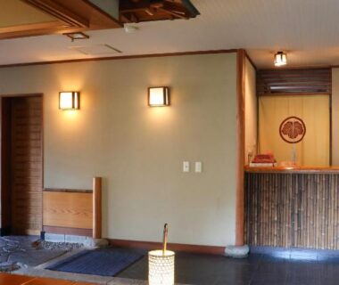 Traditional ryokan entrance with stone pathway, tatami platform, wooden reception counter and soft lantern lighting