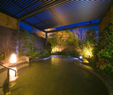Covered outdoor onsen bath with stone edge and garden lighting at Resorpia Beppu, Ōita